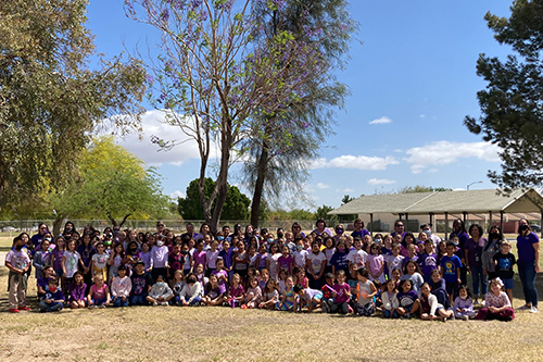 Group photo of students and teacher outside wearing purple t-shirts