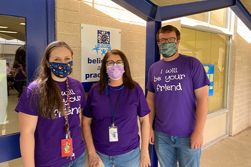 Three staff members wearing purple shirts